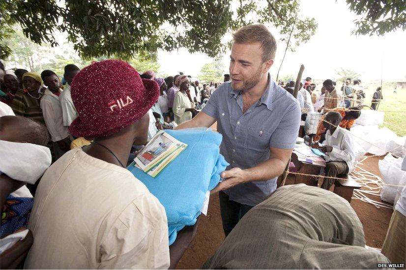 Gary Barlow offers a mosquito net to a woman