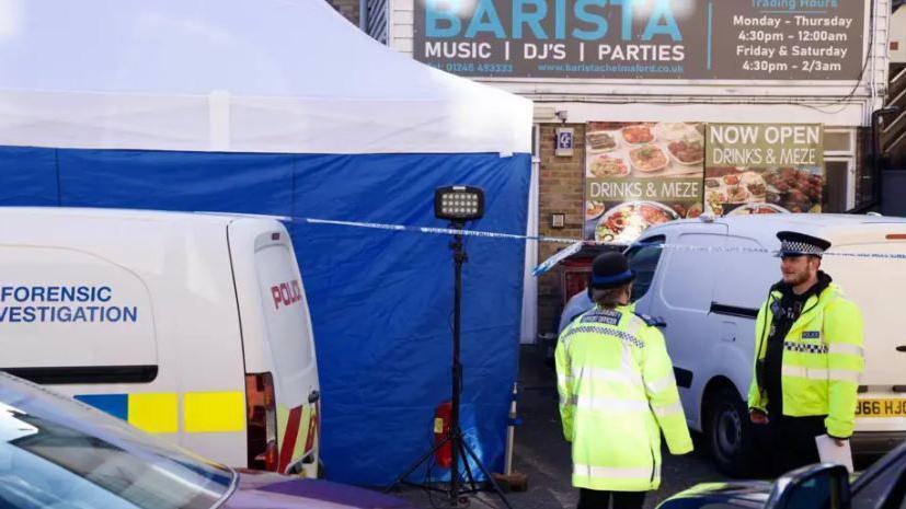 A forensic police van parked outside a shop in Chelmsford. There are two police officers wearing police uniform. 