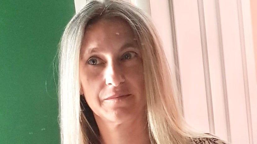 A woman with long blonde hair in front of a green wall and a white wooden door
