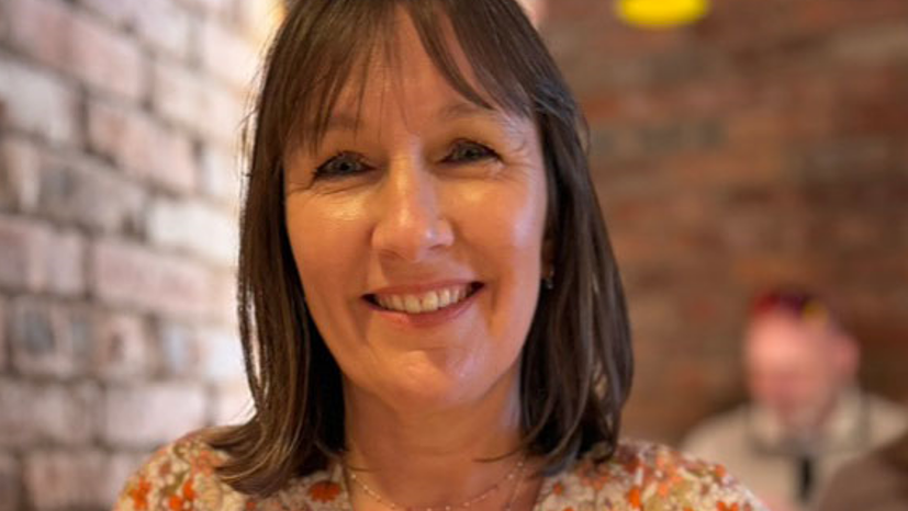 A woman with shoulder length brown hair and a flowery dress smiles at the camera
