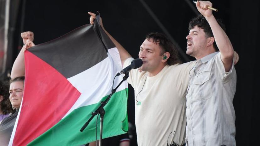 Two men and a woman on stage with a Palestinian flag between them