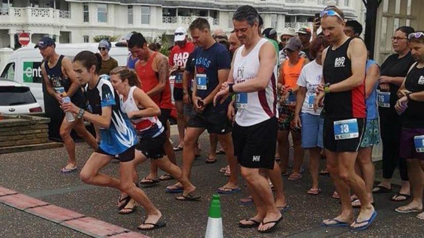 Dozens of runners wearing flip-flops at the start of a 5k on Worthing seafront.