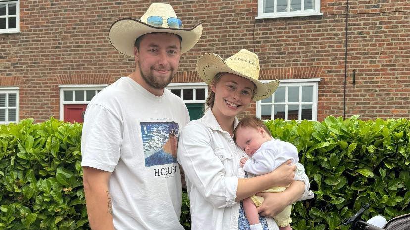 The newly engaged couple are wearing cowboy hats as they pose for a photograph, Daisy holds their baby girl.