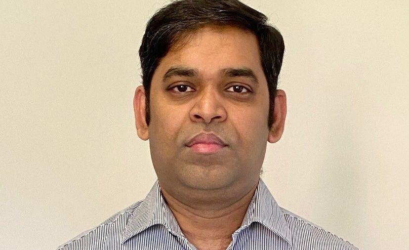 Subbu wearing a pinstripe shirt and standing against a plain background