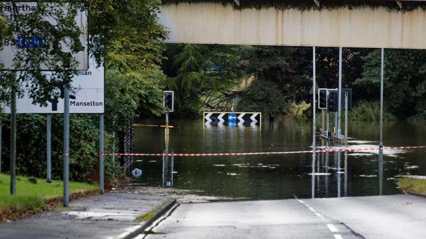 Red and white tape marks off the roundabout. Floodwater is deep ahead.