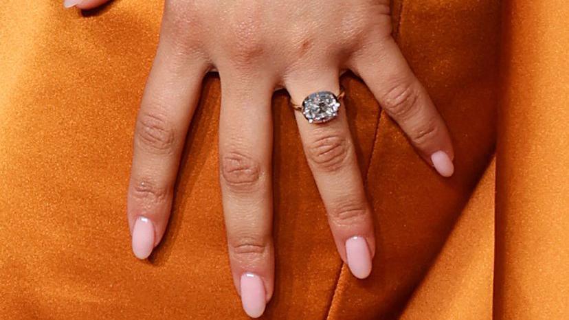 zendayas hand wearing a diamond engagement ring held against the orange fabric of her dress