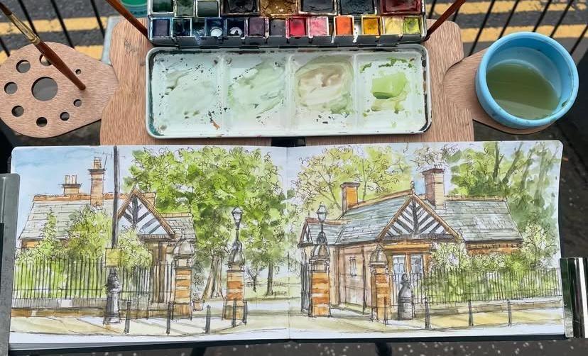 A watercolour painting of the entrance to Glasgow's Botanic Gardens. The painting is in a sketchbook and sat on an easel with paintbrushes, a water pot and a paint palette.