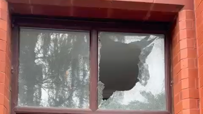 One of two windows in a red brick building has been smashed and has a large hole in it. 