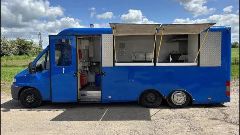 A blue food van with open shutters is parked on a clear blue day