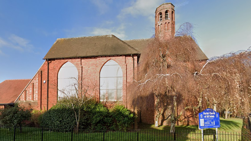 Google streetview of All Saints Church as seen from William Street in Kettering on a sunny day. The churh has large windows and a brick turret.