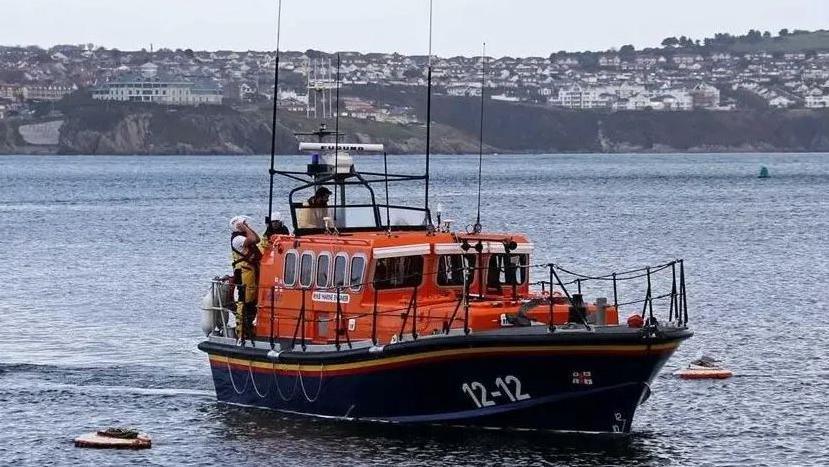 Douglas lifeboat, which is painted in the RNLI's colours of bright orange, blue, red and yellow, in Douglas Bay with Douglas in the background.