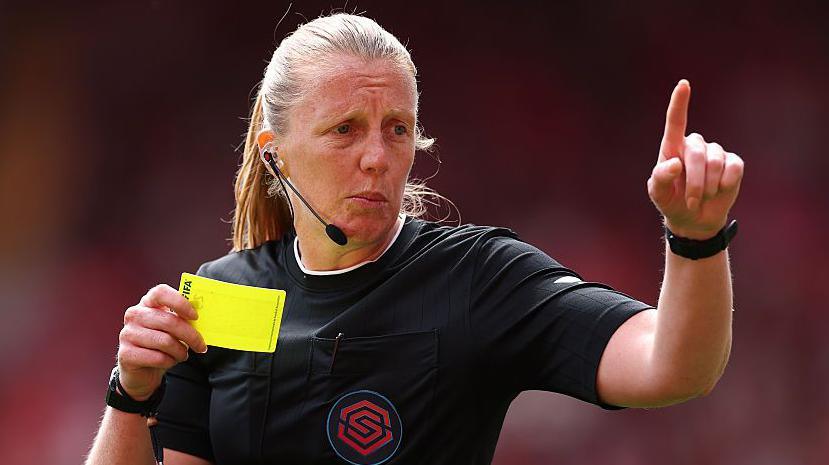 Referee Lisa Benn holding a yellow card