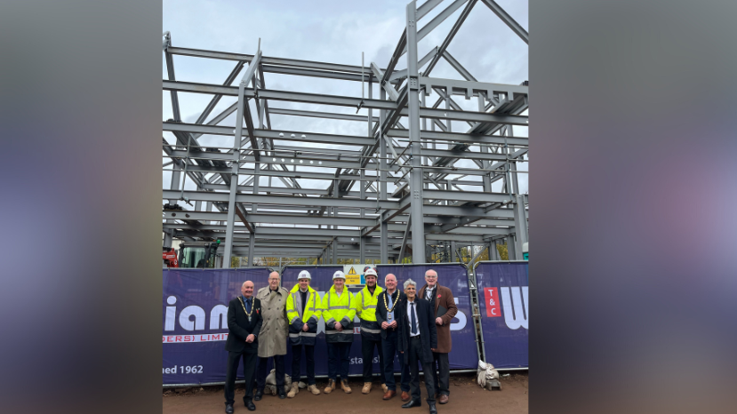 Councillors gathered infront of a large steelwork building frame. 