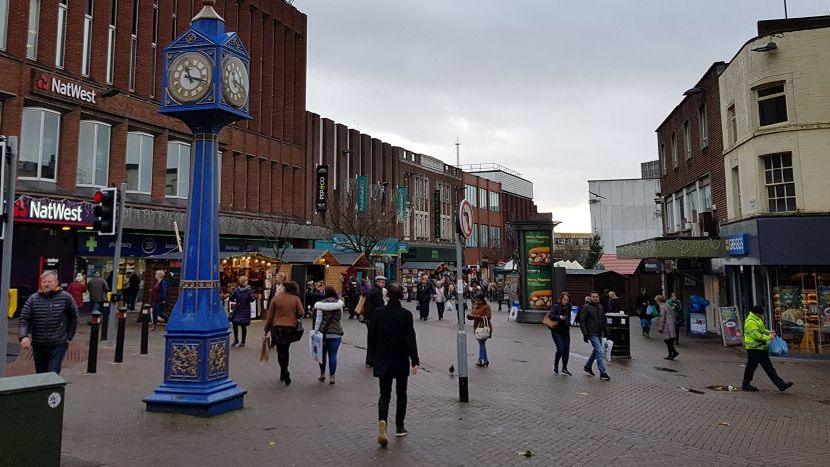 General view of Hanley town centre. Shoppers mill around by a blue clock on a post with shops in the background