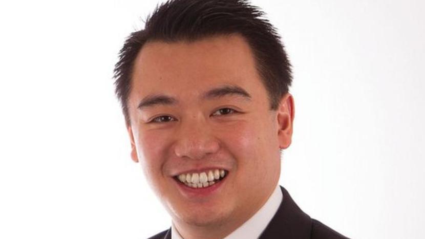 Headshot of Alan Mak smiling against a white background. You can see the top of a suit and tie.