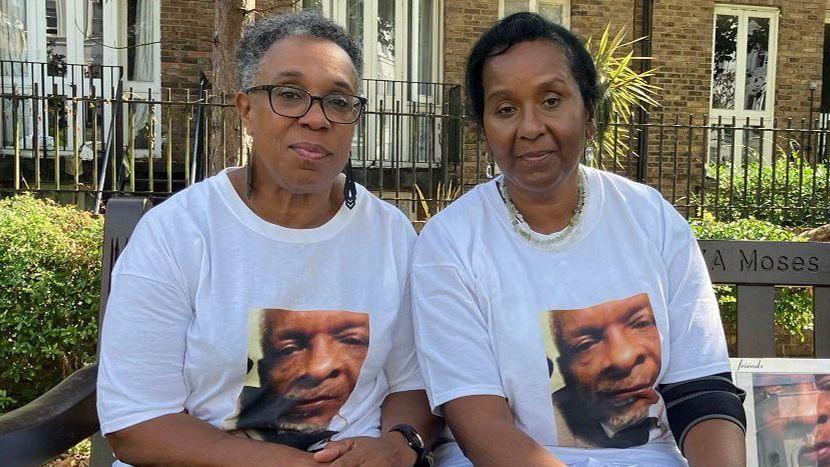 Jackie Leger (left) and Raymond's sister, Bernadette Bernard sit on a bench and look to camera. They are both wearing T shirts with Ray's face printed on them. 