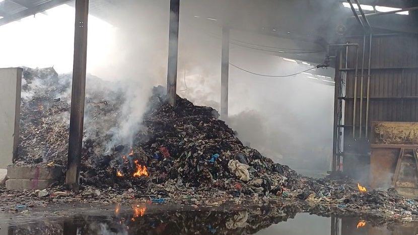 Burnt waste in a large barn. Flames still visible and lots of smoke from the pile.