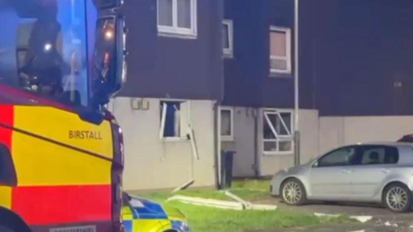 Window panes on the front of a block of flats following to explosion. There is a fire engine and a police car in the picture.