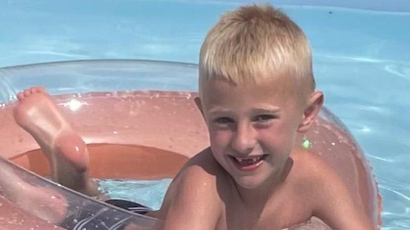 Freddie Farrow, who is blond, smiling and floating on an inflatable doughnut in a swimming pool.