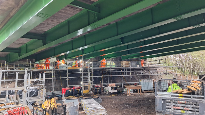 Contractors in hi vis clothing on scaffolding inspect the underside of a green bridge