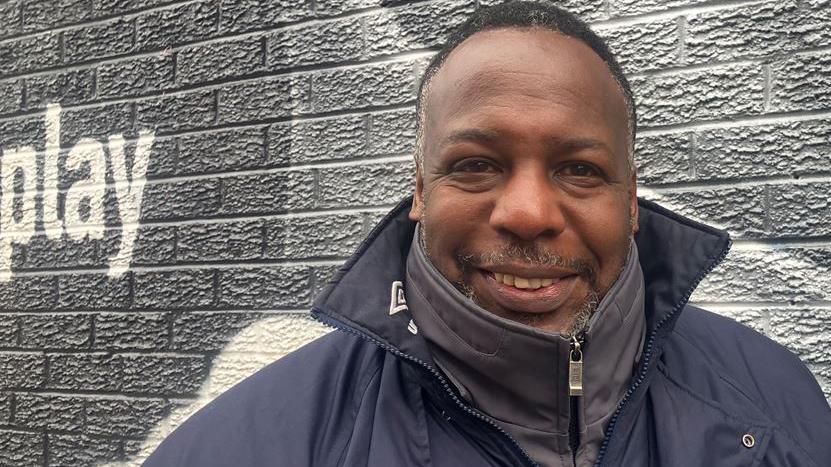 Lloyd Watson, wearing a black waterproof zip-up jacket, in front of the Marcus Rashford mural. 