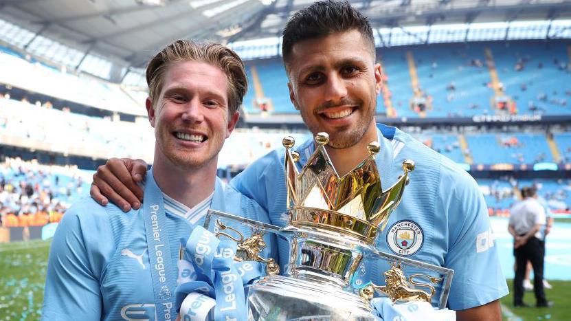 Kevin de Bruyne and Rodri holding the Premier League trophy in 2024