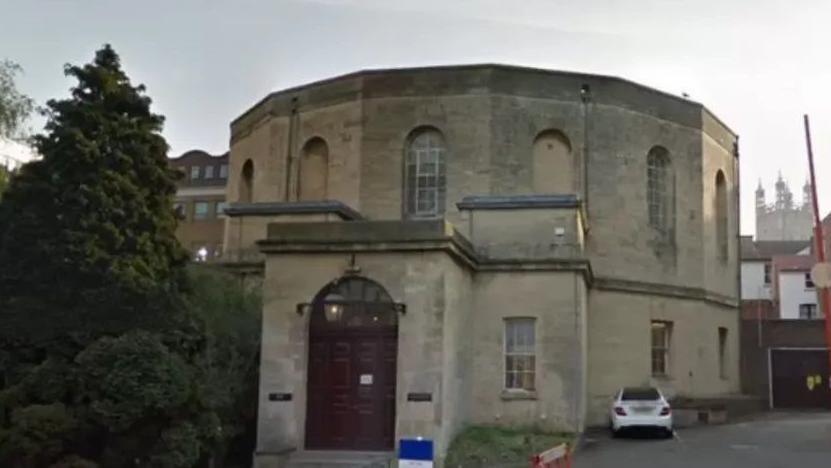 A Google Maps streetview picture of Gloucester Crown Court. The building is an unusual round shape, with large arched windows and a flat roof. 