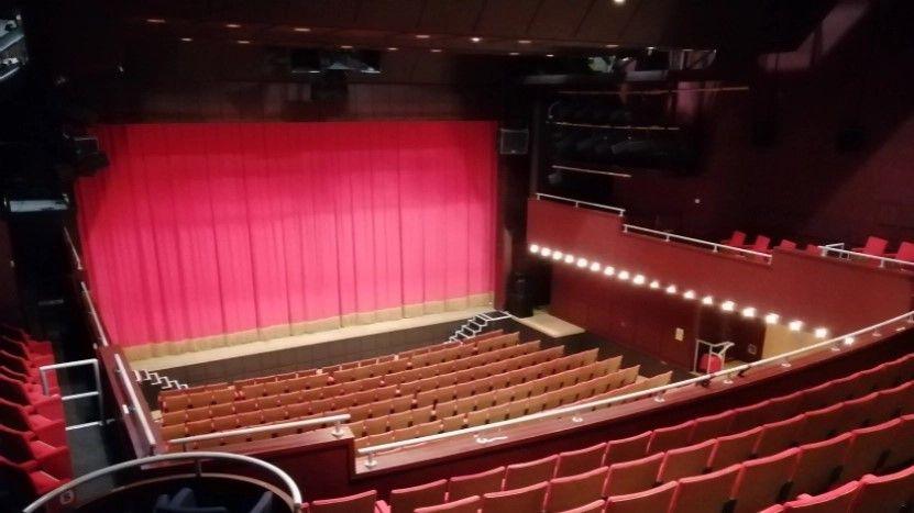 The interior of the theatre with empty chairs in the auditorium and a red curtain at the front of the stage