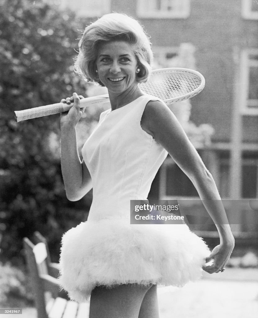 Pericoli is holding a racquet and is wearing a white dress trimmed with feathers