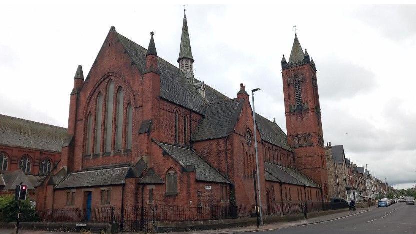 The Grade II listed Church of St Paul, in St Paul's Road, Hartlepool, from the road with its windows boarded up. It is a red brick-built building.
