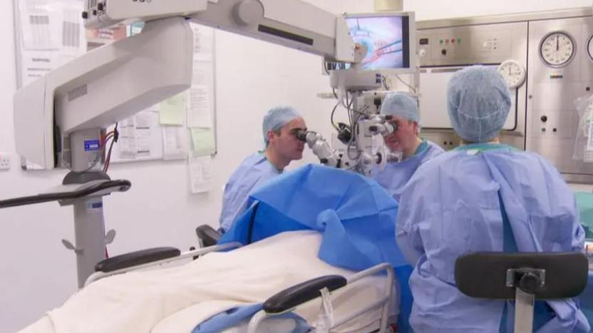 Three surgeons wearing gowns carry out a procedure in a hospital operating theatre