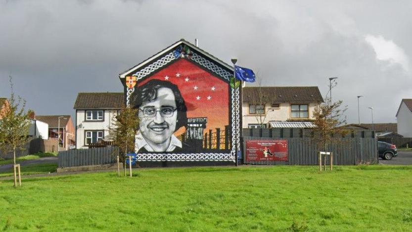 A grassy area where the paramilitary commemoration took place in front of a mural of the former INLA prisoner Michael Devine in the Galliagh area of Derry