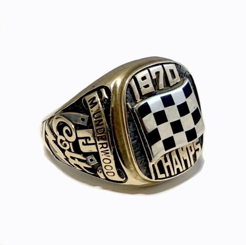 A gold and black signet ring with the words '1970 CHAMPS' on the front with the name 'M.UNDERWOOD' on the side.