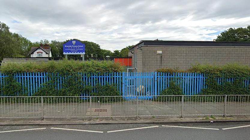 The exterior of Riverside Primary School in Seacombe with blue fencing and a blue sign 