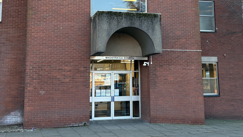 The entrance to Ipswich Magistrates' Court. Brown brick walls can be seen either side of a glass doorway.