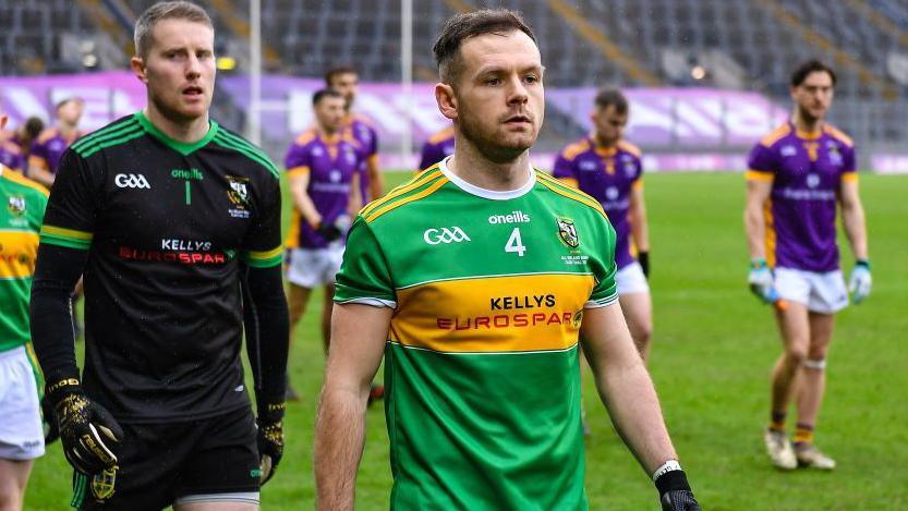 A man with brown hair wearing a green and yellow jersey