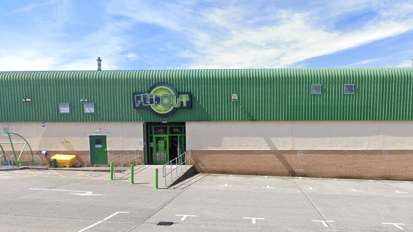 The Flip Out building from the outside. It is an industrial building with a green roof. The Flip out logo is above the green entrance.