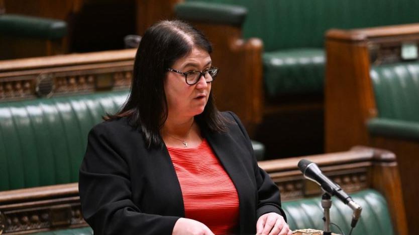Rachel Hopkins MP in the House of Commons. She is wearing a red top with a black blazer over the top and is talking into a microphone at the despatch box.