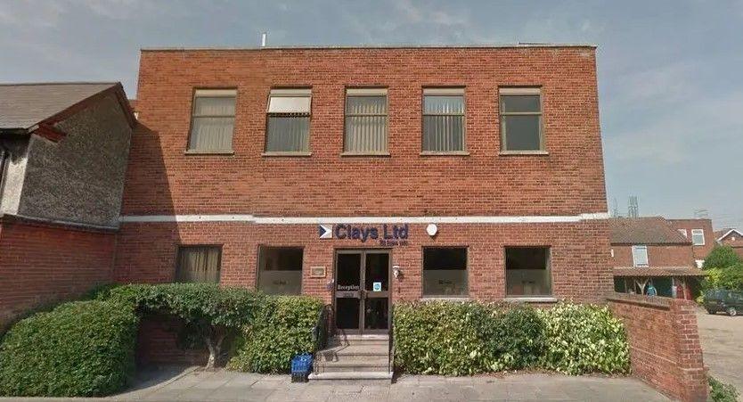 The red brick facade of the head office of Clays in Bungay with large windows, brown doors and concrete steps 