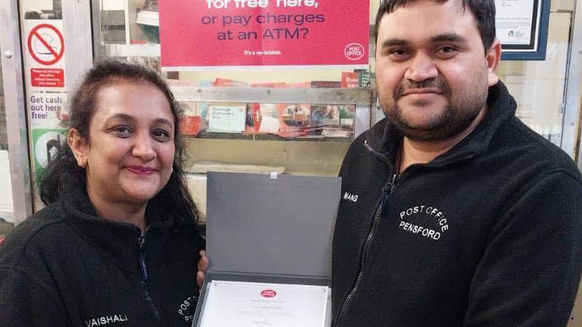 A ma and a woman wearing fleeces with Post Office Pensford written on them