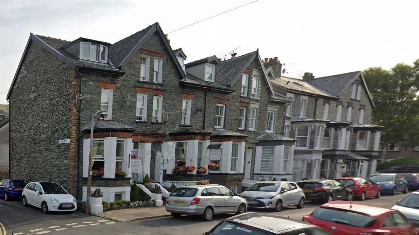 Harvington House in Keswick. The guest house is an end of terrace property with bay windows, dormer windows, slate cladding and white detailing. Every parking space on the street and a side street off it has been taken.