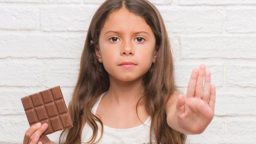 Girl holding up a piece of chocolate in one hand and making a stop sign with the other. 