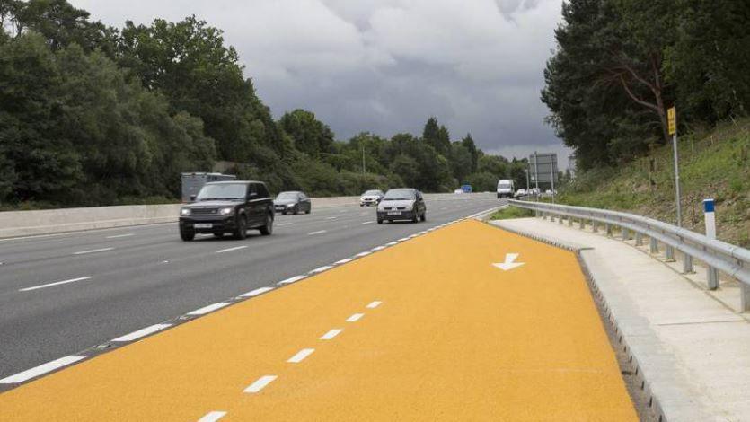 A view of an emergency area along the M1. The new area is yellow in colour and is sat at the side of the four-lane carriageway.