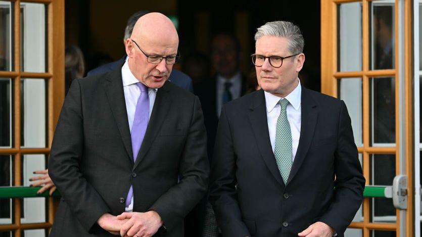 First Minister John Swinney (a bald man with glasses, wearing a dark suit) in conversation with Sir Keir Starmer (a man with grey hair and glasses, also wearing a dark suit)