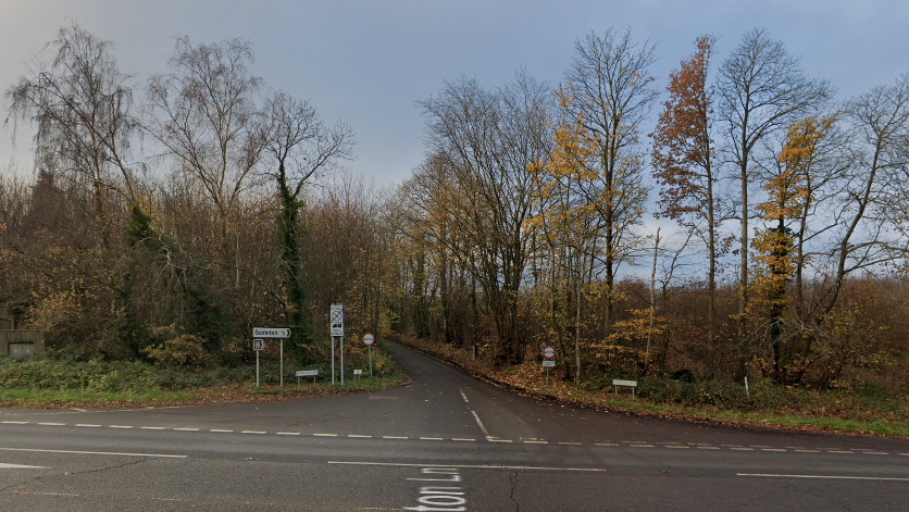 A Google street image from the side of a main road looking down a lane with trees along the roadside