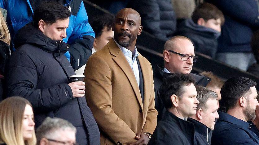 Jason Roberts stands watching a game at The Hawthorns wearing a camel coloured overcoat