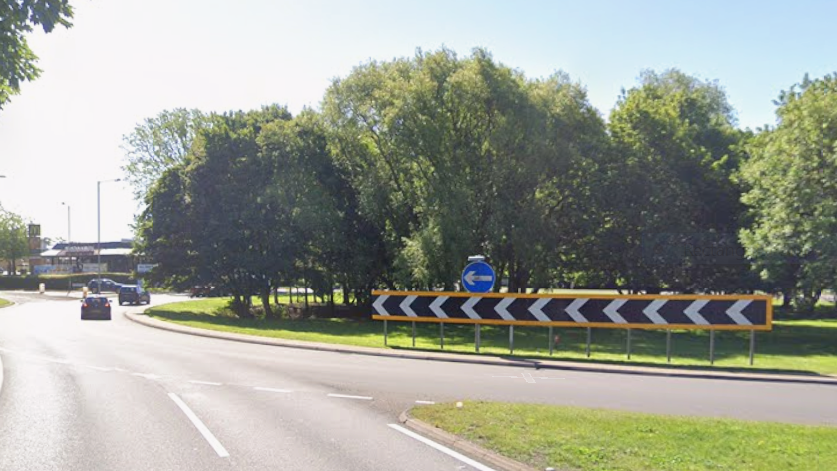 A Google Maps street view image of the approach to a roundabout. A car is driving on the left of the image and a McDonald's is in the distance.