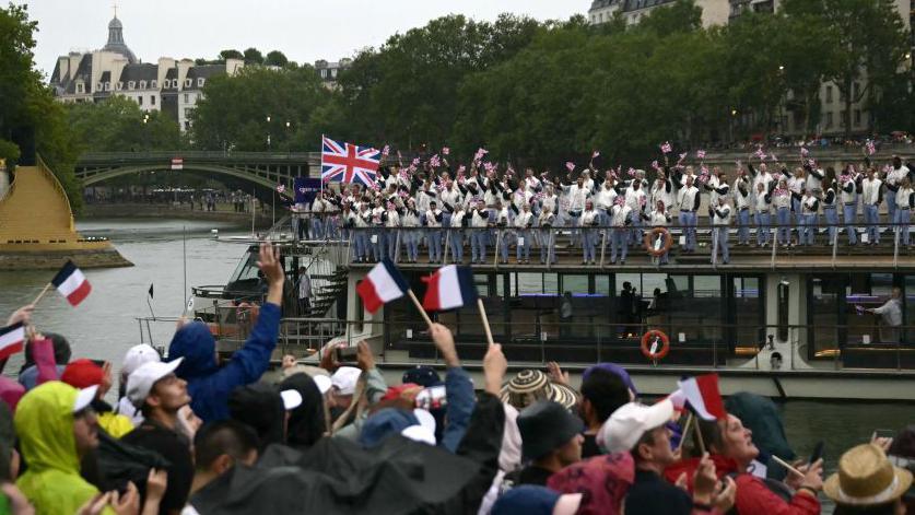 Crowds watch a boat go past on the River Seine with the Team GB athletes on