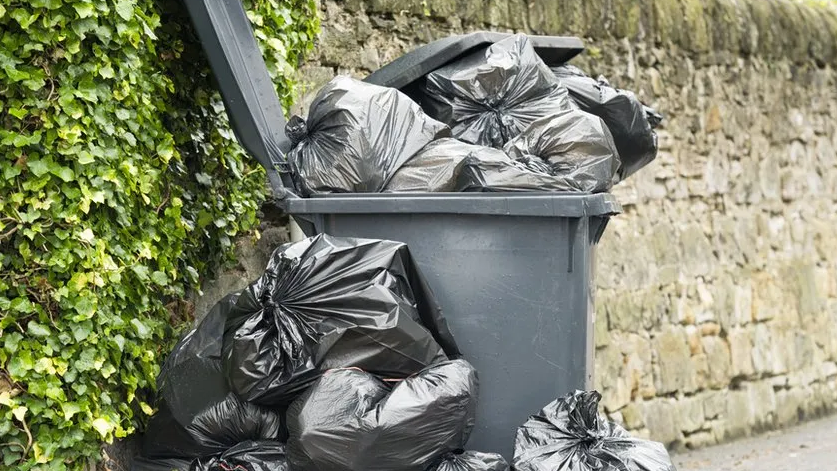 Black bags in and out of a wheelie bin on a pavement 