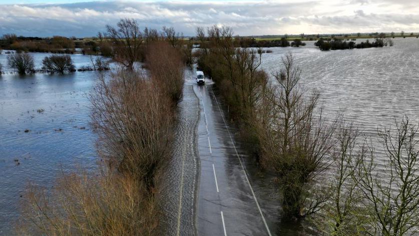 An aerial picture of a flooded Welney Wash road, which a large white van is attempting to cross. 